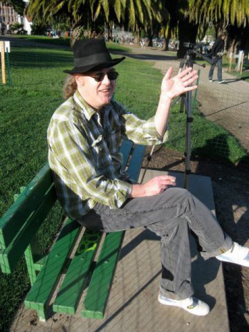 a an sits on a park bench and waves and smiles at the camera